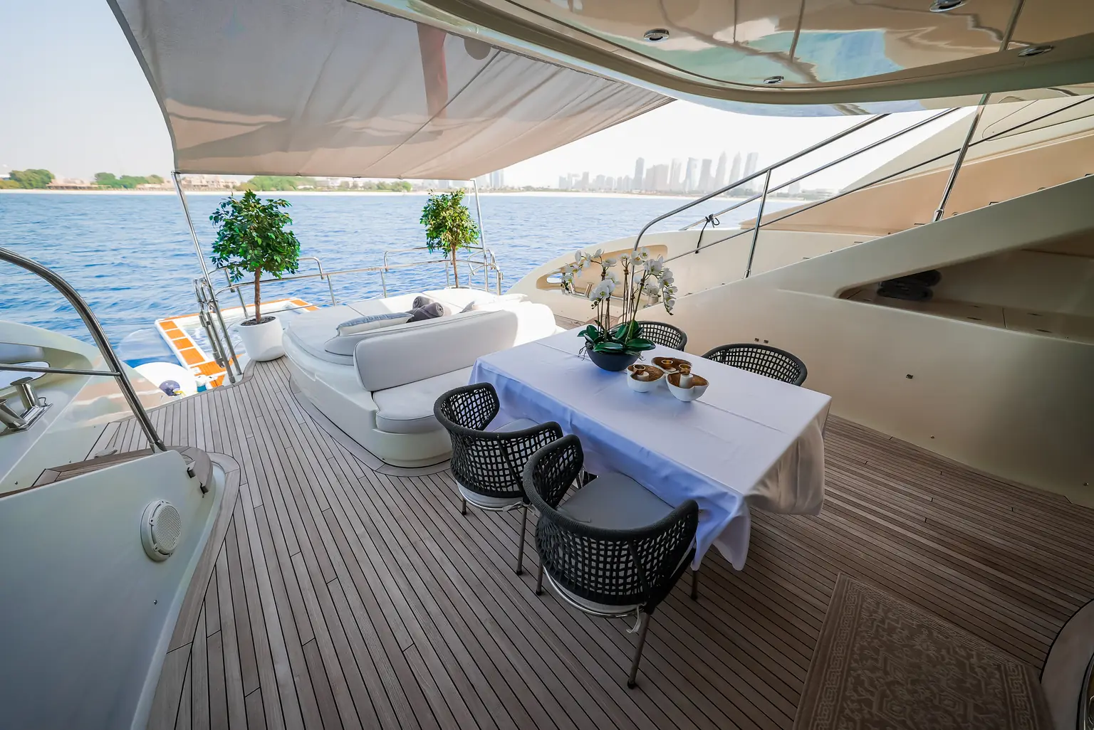 Aft deck table set between potted olive trees with the Dubai skyline beyond