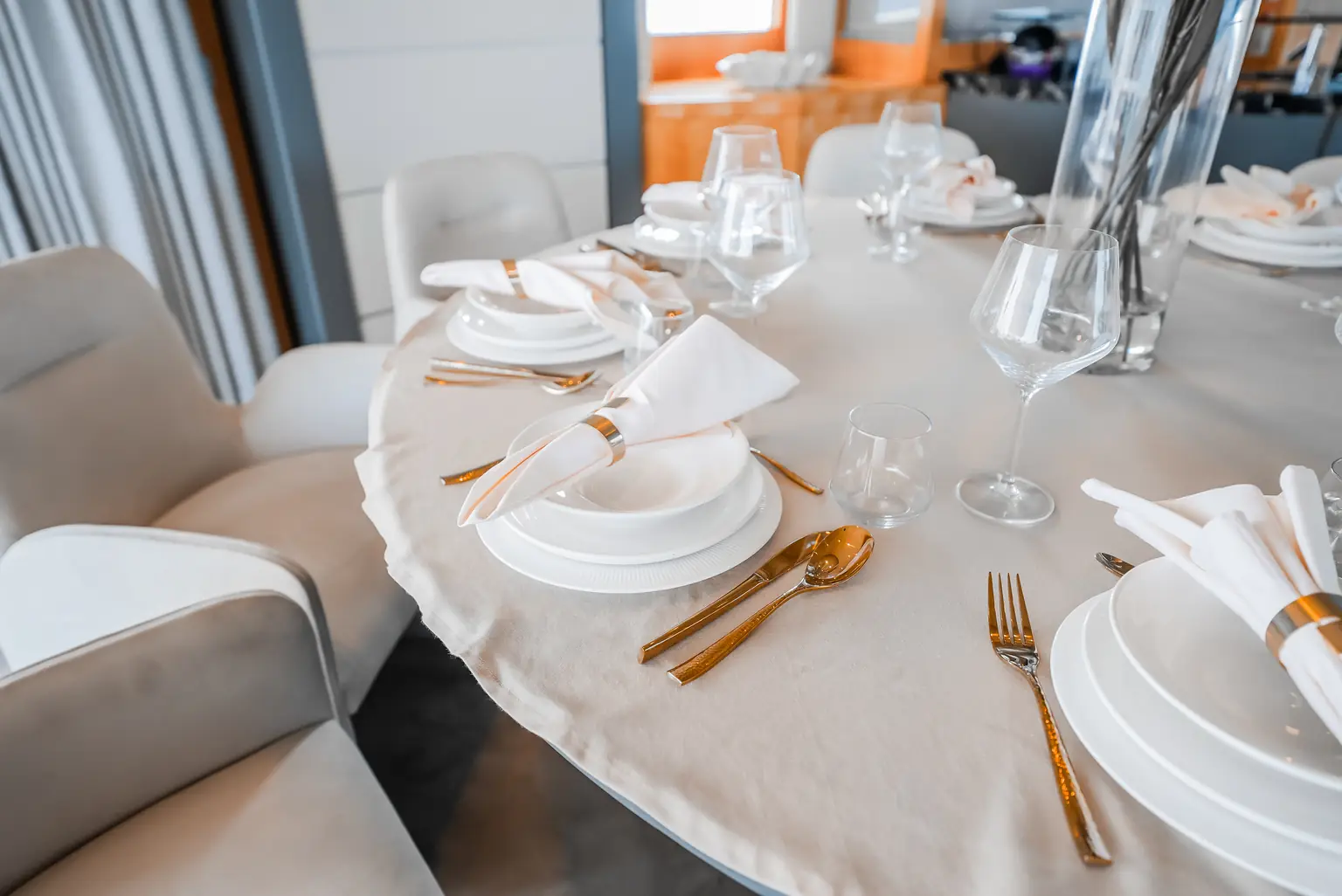 Place setting on the dining table with gold cutlery, folded linen and crystal glassware